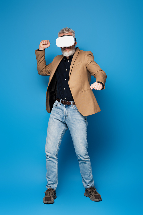 full length of middle aged man in vr headset gesturing on blue