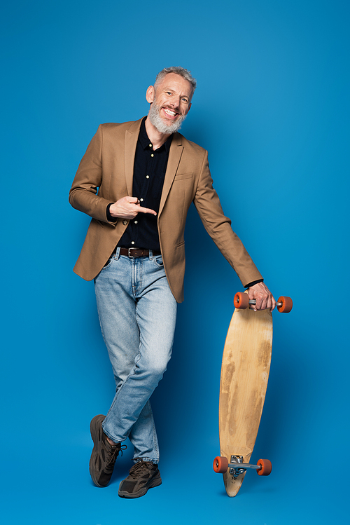 full length of pleased middle aged man pointing at longboard on blue