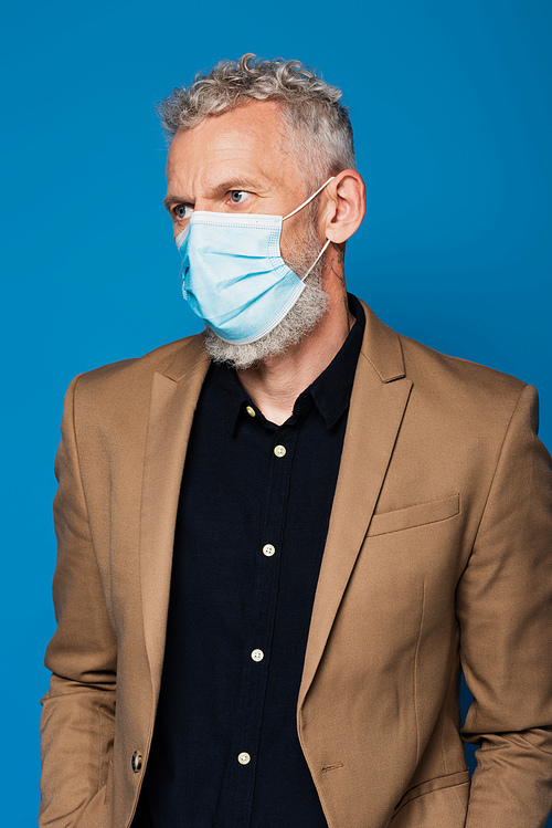 middle aged man in medical mask looking away isolated on blue