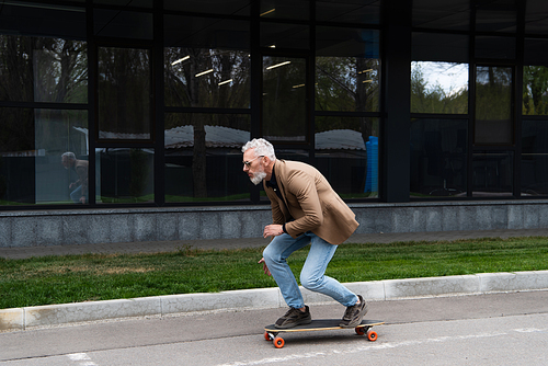 full length of bearded middle aged man in sunglasses riding longboard outside