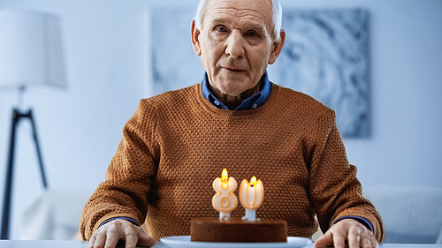 lonely elderly man sitting in front of birthday cake with candles and  in living room