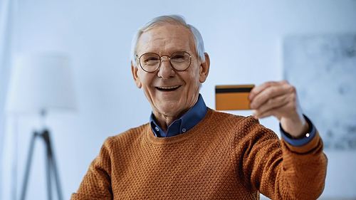 smiling elderly man in glasses holding credit card in modern living room