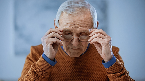 concentrated elderly man adjusting glasses on grey background