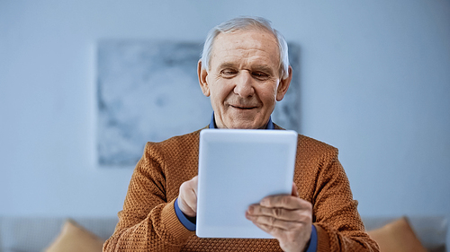 smiling elderly man using tablet in modern living room