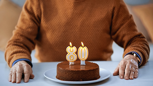 partial view of elderly man sitting in front of birthday cake with candles at home