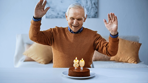 joyful elderly man celebrating birthday in front of cake with burning candles in living room