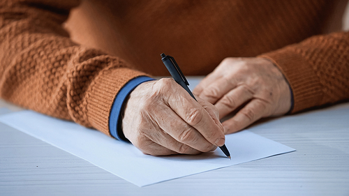 close up view of male elderly hands writing on empty blank with pen