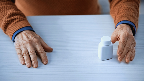cropped view of medicine jar on table between hands of elderly man on grey background