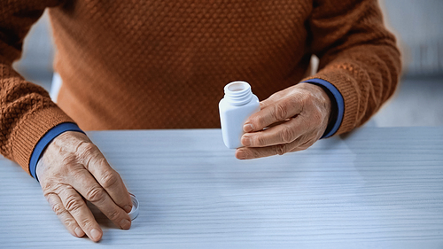 cropped view of open medicine jar in hand of elderly man on grey background