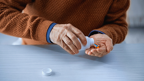 cropped view of medication jar and multicolored pills in hands of senior man on grey background