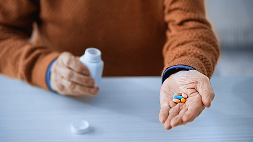 close up view of medicine jar and multicolored pills in hands of elderly man on grey background