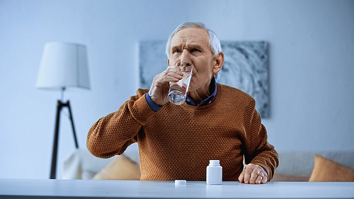 elderly man taking medication and drinking water in living room