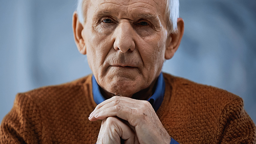portrait of elderly man with clenched hands near face on grey background