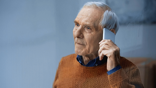 sad elderly man speaking on cellphone on grey background behind rainy glass