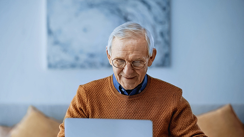 smiling elderly man working on laptop in modern living room