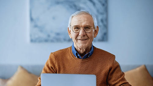 smiling elderly man sitting with laptop at home