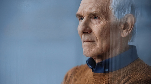 portrait of elderly man looking away through rainy window on grey background