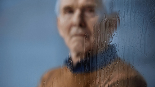 blurred portrait of elderly man  through rainy window on grey background