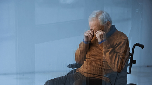 senior man in . covering eyes with hands on grey background behind rainy glass