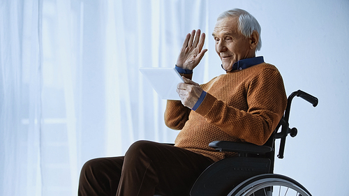 cheerful pensioner in . waving hand and having video call on tablet at retirement home