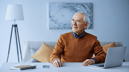 elderly man sitting at table with laptop and smartphone at home