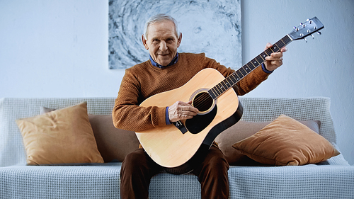 smiling elderly man sitting on sofa with guitar in living room