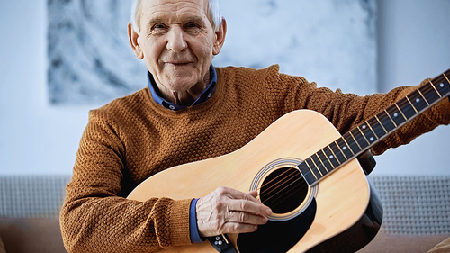 cheerful elderly man sitting on sofa with guitar in living room