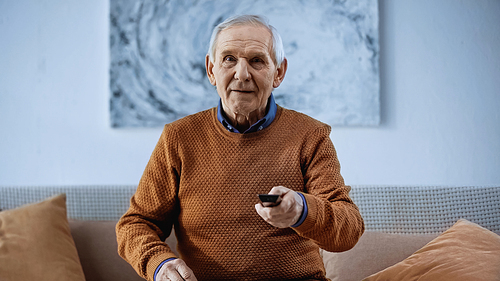 focused senior man sitting on sofa with tv remote controller and  at home