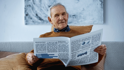 senior man sitting on sofa and reading newspaper at home