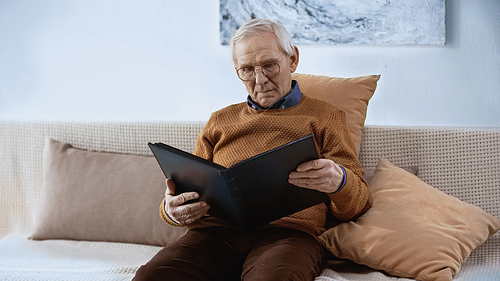 elderly man sitting on sofa with family album at home