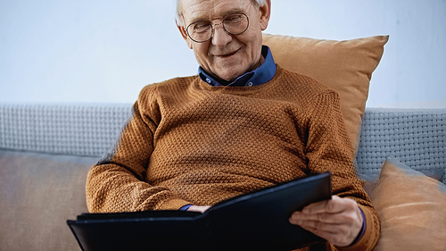 happy elderly man sitting on sofa with family album in living room