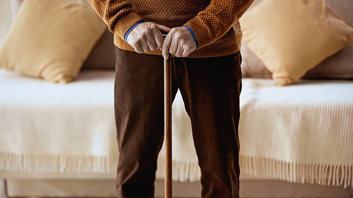 cropped view elderly man with walking stick standing near sofa at home