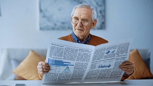 elderly man in glasses reading newspaper at modern living room
