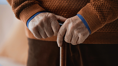 close up view of elderly male hands holding walking stick on blurred orange background