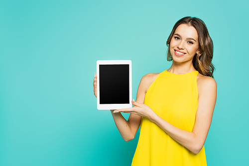 Positive woman in yellow dress showing digital tablet with blank screen isolated on blue