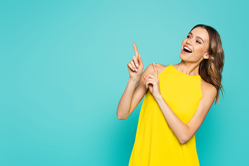 Smiling woman in yellow dress pointing with fingers isolated on blue