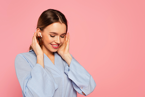 Pretty woman smiling while listening music in earphone isolated on pink