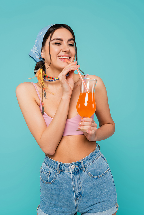 Pretty woman in top and bandana drinking cocktail isolated on blue