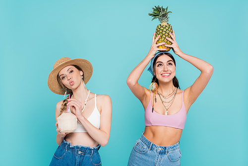 Pretty women holding pineapple and cocktail in coconut isolated on blue