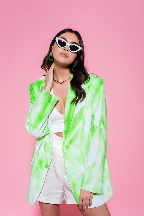 Stylish woman in sunglasses and jacket posing on pink background