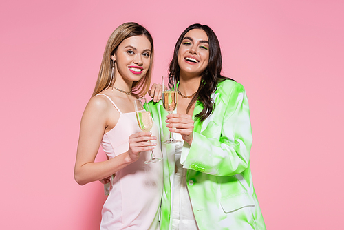 Pretty friends with champagne smiling at camera on pink background