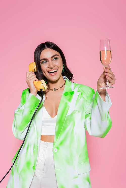 Pretty woman talking on telephone and holding glass of champagne isolated on pink