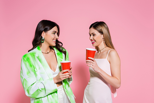 Young friends holding plastic cups on pink background