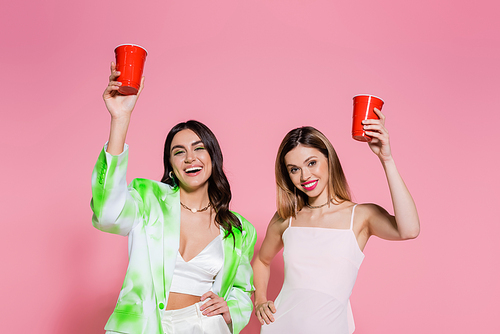 Cheerful friends holding plastic cups on pink background