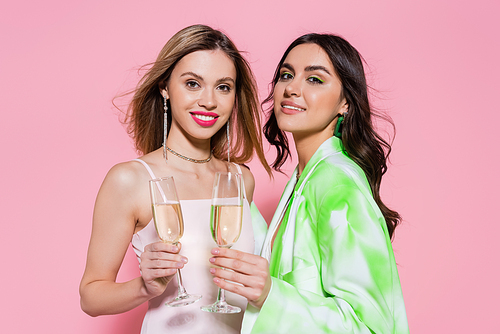 Smiling friends holding glasses of champagne and  on pink background