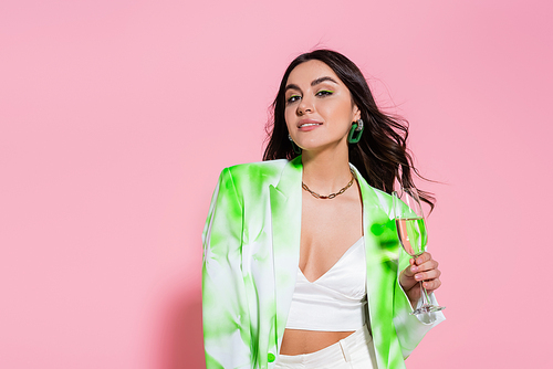 Brunette woman in blazer holding glass of champagne on pink background