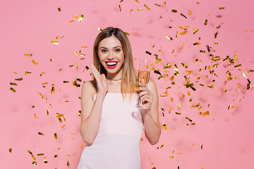 Pretty woman with champagne  near golden confetti during party on pink background