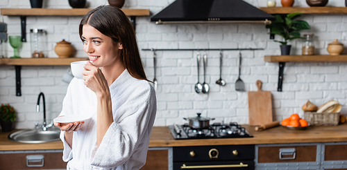 smiling young adult woman in bathrobe drinking coffee in modern loft, banner