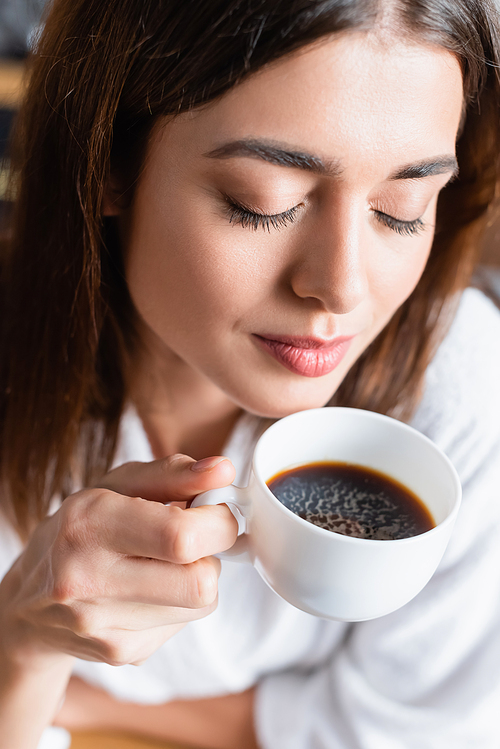 high angle view of young adult woman drinking coffee with closed eyes on blurred background