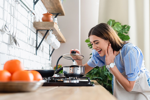 happy young adult woman cooking near burner in modern kitchen